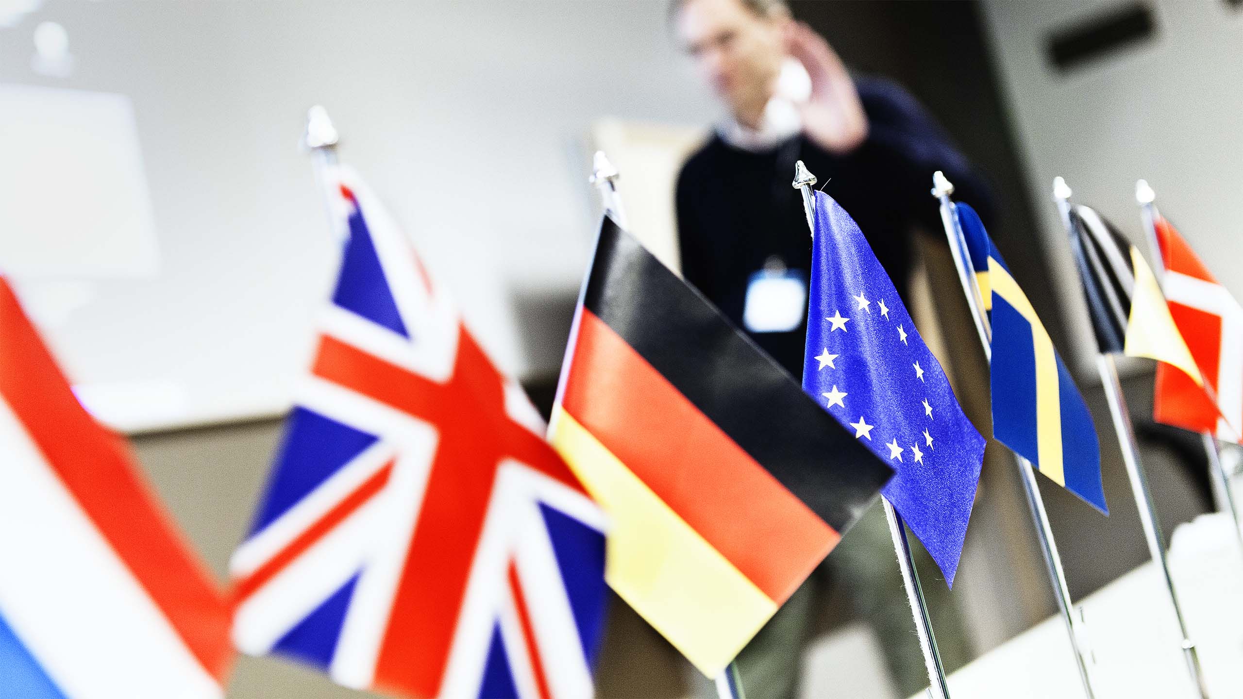 Mindre flaggstångar står uppradade på ett bord. Flaggor från Nederländerna, Storbritannien, Tyskland, EU, Sverige, Berlin och Danmark.