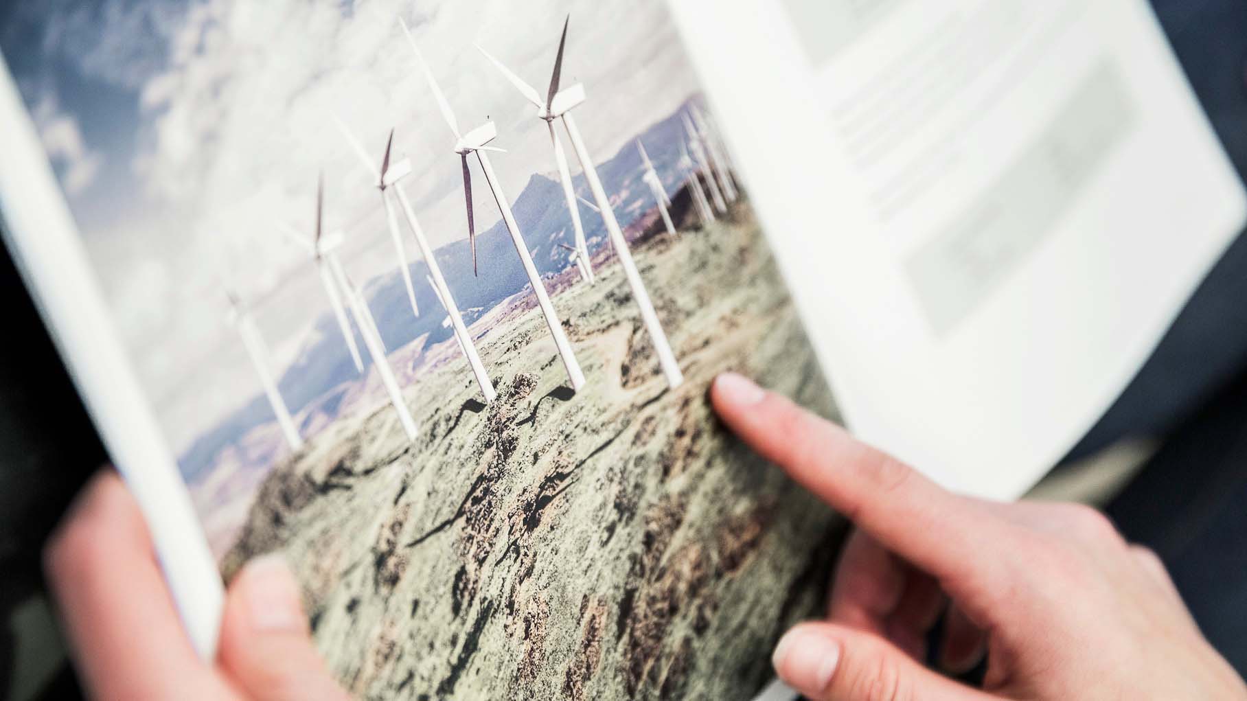 Uppslagen katalog med bild på flera vindkraftverk som står på ett fält. En hand som pekar på bilden.